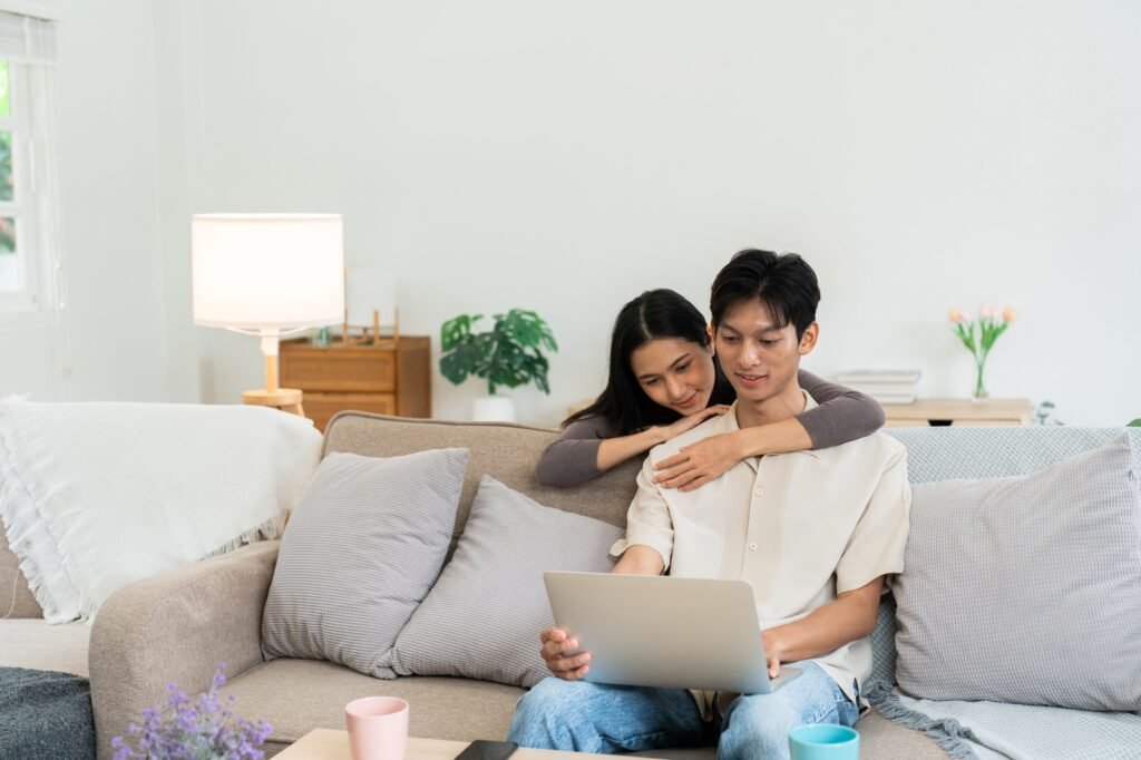 Happy young couple looking laptop relax on sofa in living room watch video on laptop together